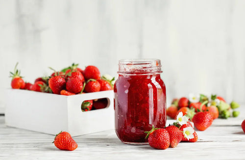 Confiture de fraises maison rouge et brillante, dans un pot en verre avec des fraises fraîches autour.