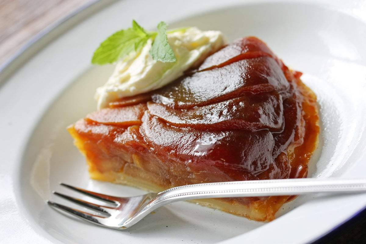 Tarte Tatin dorée et caramélisée garnie de pommes renversées sur une pâte feuilletée, servie sur une assiette.