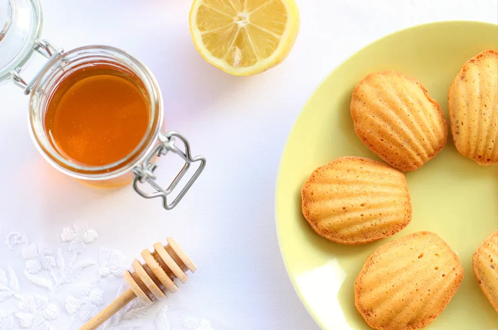 Madeleines dorées au miel et citron, disposées dans un plat, avec une tasse de thé fumante à côté.