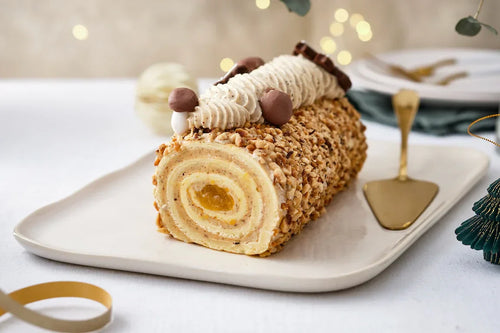 Bûche de Noël roulée à la crème de marrons, recouverte de noisettes caramélisées et décorée de rosaces de crème et de marrons glacés.