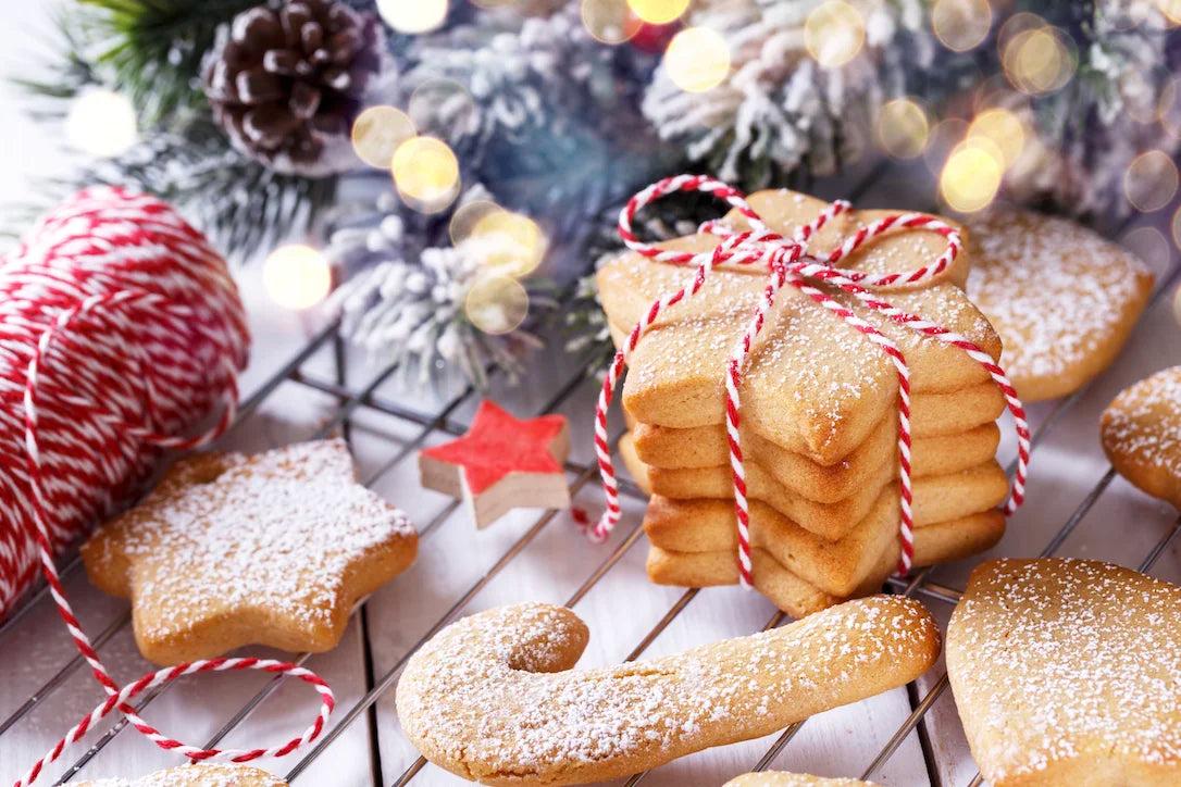 Assiette de sablés de Noël en forme d’étoiles et de sapins, décorés de glaçage blanc et saupoudrés de sucre glace.