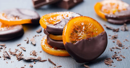Tranches d’orange confite nappées de chocolat noir brillant, disposées sur une grille.