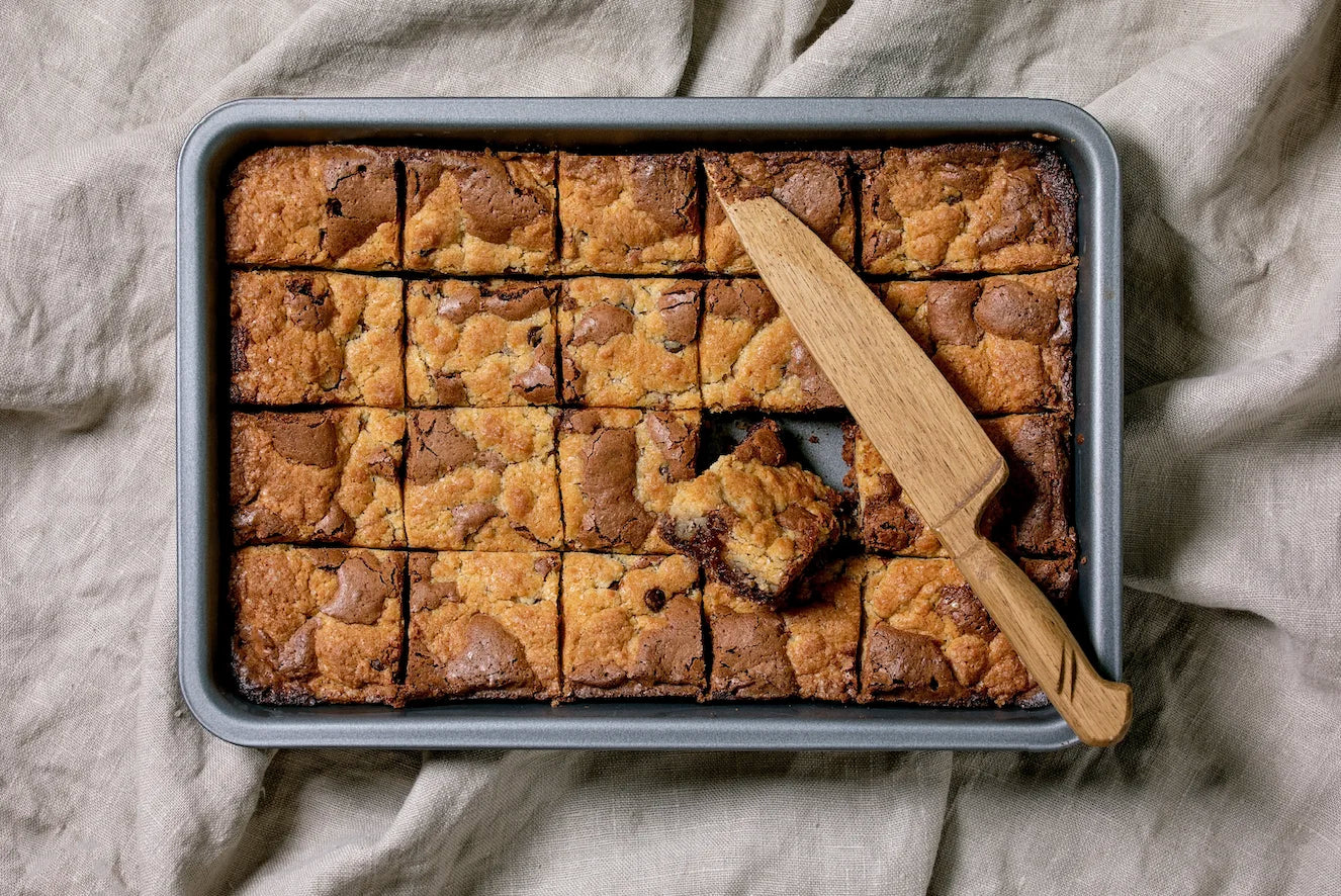 Carrés de brookie maison, moitié brownie fondant, moitié cookie doré, posés sur une planche en bois.