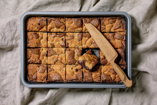 Carrés de brookie maison, moitié brownie fondant, moitié cookie doré, posés sur une planche en bois.