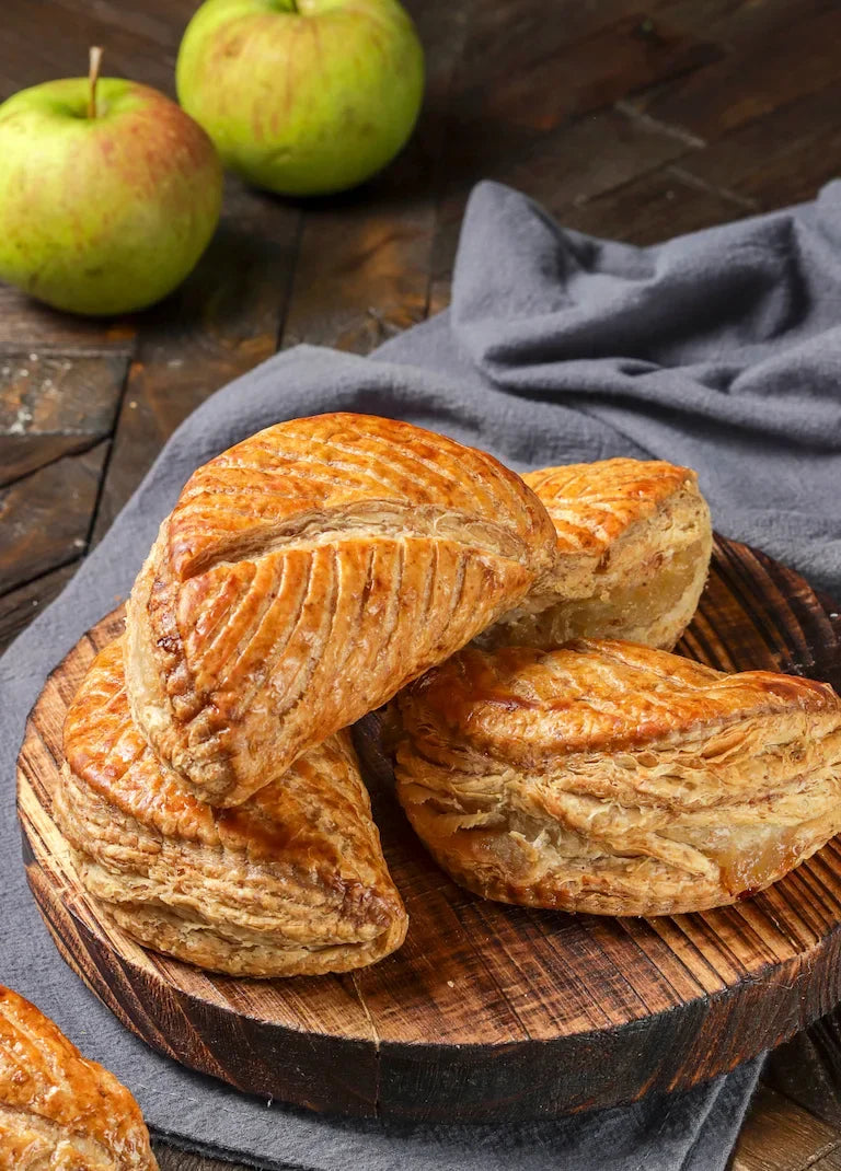 Chaussons aux pommes maison dorés, feuilletés, garnis de compote de pommes, posés sur une plaque de cuisson.