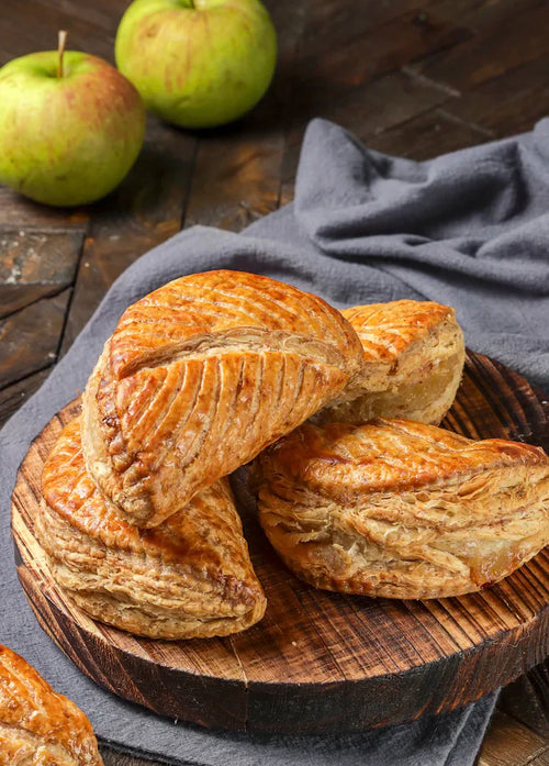 Chaussons aux pommes maison dorés, feuilletés, garnis de compote de pommes, posés sur une plaque de cuisson.