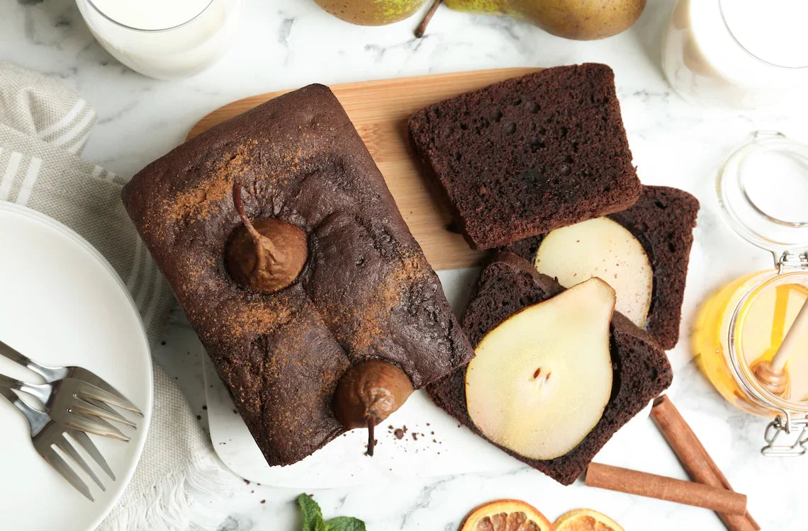 Gâteau fondant au chocolat avec poires entières pochées visibles à la coupe, nappé d’un sirop brillant.