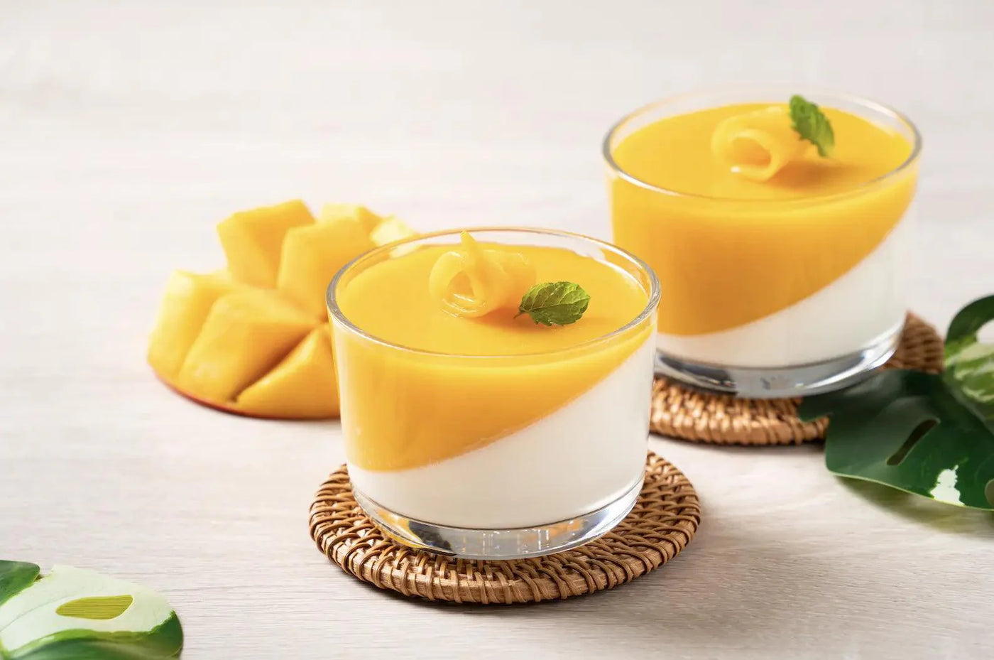 Une image de panna cotta à la mangue dans un ramequin transparent, garnie de coulis de mangue et de petits morceaux de mangue fraîche sur le dessus.