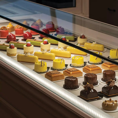 Vitrine pâtisserie avec alignement d’entremets sur semelles noires